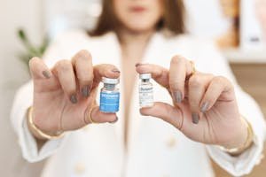 A close-up of a woman holding Xeomin and Dysport vials, showcasing cosmetic treatment options.