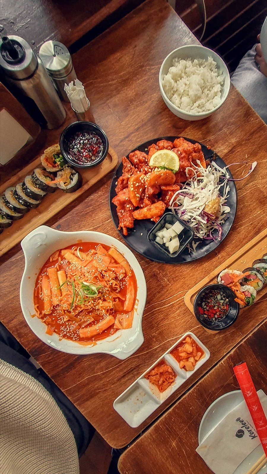 Korean meal on a wooden table with kimchi and pickled radish side dishes, the kind of banchan you can refill for free