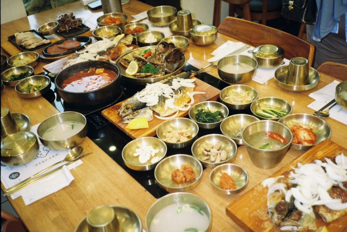 Korean restaurant table covered with banchan side dishes, soup, and grilled fish, a typical Korean restaurant meal
