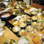Korean restaurant table covered with banchan side dishes, soup, and grilled fish, a typical Korean restaurant meal
