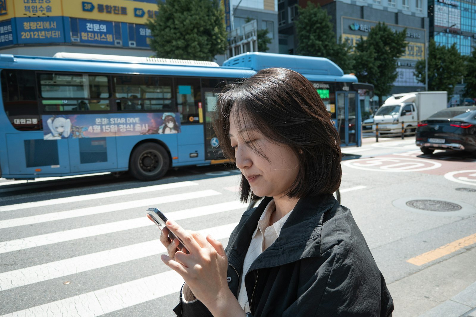 A woman checking her smartphone at a crosswalk in Seoul, where many apps ask for Korean phone number verification